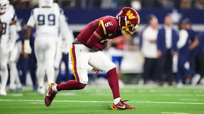 American football player in burgundy and gold uniform sprinting on a green field during a game with blurred opponents in the background.