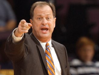 Man in a suit with orange striped tie points toward the audience while speaking passionately on stage or at a podium.