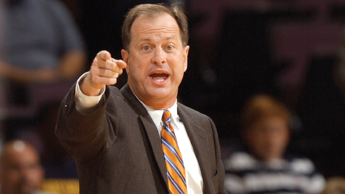 Man in a suit with orange striped tie points toward the audience while speaking passionately on stage or at a podium.