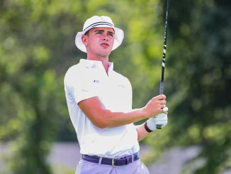 Golfer in a white polo and hat watches the ball mid-swing on a sunny course with a golf club raised high.