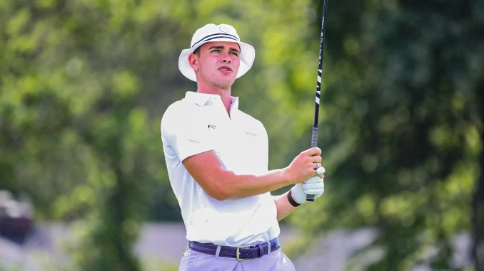 Golfer in a white polo and hat watches the ball mid-swing on a sunny course with a golf club raised high.