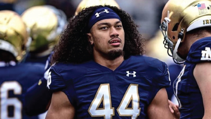 Football player in blue jersey with number 44 and long curly hair, standing on the field during a game.