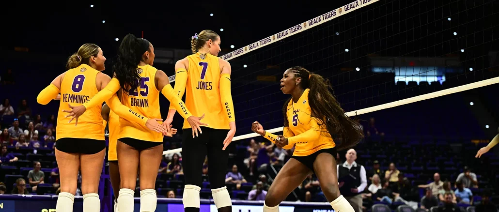 Volleyball players in yellow uniforms huddle on the court near the net during a match.