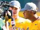 Two baseball players in yellow uniforms are interviewed by a reporter holding an ESPN microphone; both wear National Champions hats.