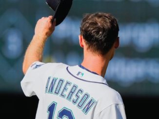Baseball player facing away, lifting his cap in celebration on the field, jersey reads 'ANDERSON' and number 12 on the back.