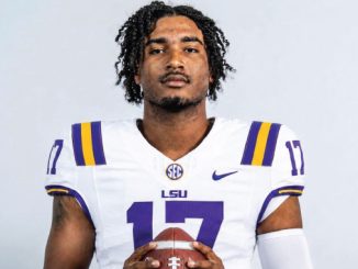 LSU football player wearing number 17 jersey poses with a football, looking at the camera
