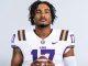 LSU football player wearing number 17 jersey poses with a football, looking at the camera