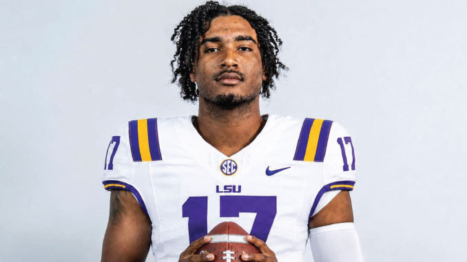 LSU football player wearing number 17 jersey poses with a football, looking at the camera