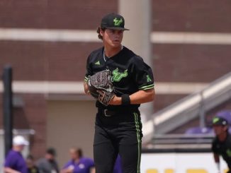 Male baseball pitcher in black and green uniform on the mound, glove held ready for a pitch.