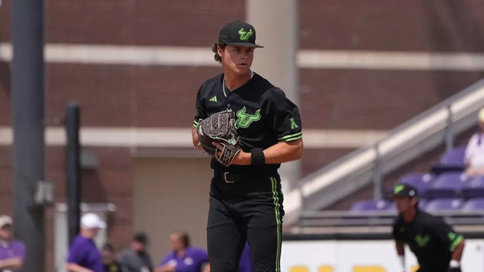 Male baseball pitcher in black and green uniform on the mound, glove held ready for a pitch.