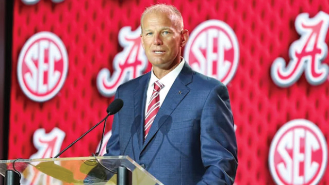 Man in a blue suit giving a speech at a podium with an SEC-branded red backdrop, speaking into a mic.