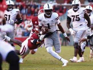 Running back in white with the ball evades red-clad defenders during a college football play.