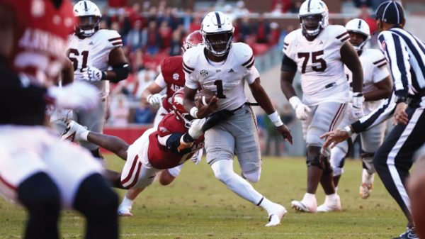 Running back in white with the ball evades red-clad defenders during a college football play.