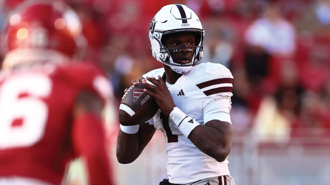 Quarterback in a white uniform holding a football, poised to throw, on a football field with red-clad defenders nearby.