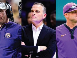 Three LSU football coaches in purple: left with headset, middle in a suit with arms crossed, right in a polo and cap.