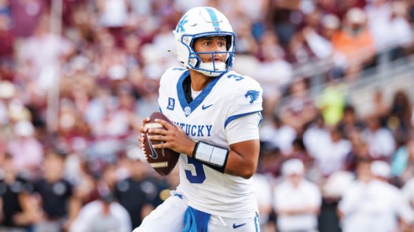 Kentucky quarterback in white and blue jersey #3 holding the football and looking downfield during a game.