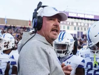 Football coach wearing a headset and gray hoodie speaks to Georgia State Panthers players on the sideline.