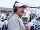 Football coach wearing a headset and gray hoodie speaks to Georgia State Panthers players on the sideline.