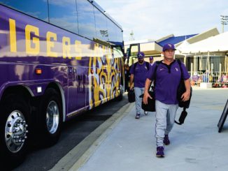 Purple team bus with tiger artwork parked at a stadium as players in purple uniforms walk toward the arena.