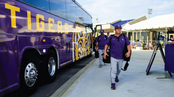 Purple team bus with tiger artwork parked at a stadium as players in purple uniforms walk toward the arena.