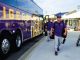 Purple team bus with tiger artwork parked at a stadium as players in purple uniforms walk toward the arena.
