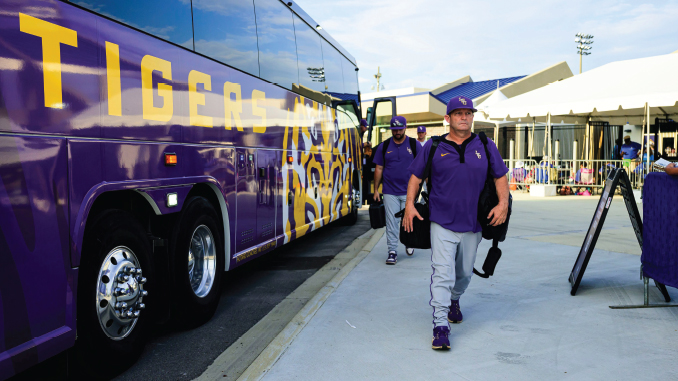 Purple team bus with tiger artwork parked at a stadium as players in purple uniforms walk toward the arena.
