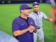 Coach in a purple LSU polo speaks to his team on a baseball field, players gathered around him.