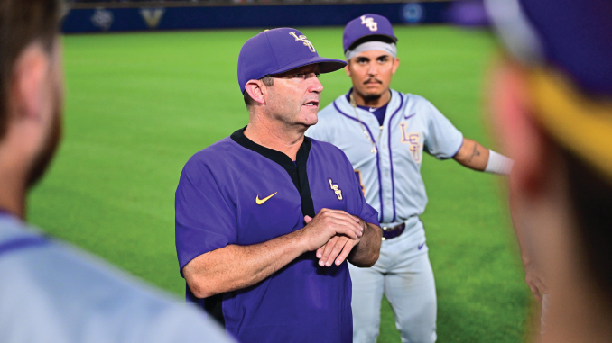 Coach in a purple LSU polo speaks to his team on a baseball field, players gathered around him.