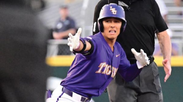 LSU Tigers baseball player in a purple uniform slides toward base with arms outstretched as an umpire watches the play.