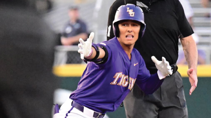 LSU Tigers baseball player in a purple uniform slides toward base with arms outstretched as an umpire watches the play.