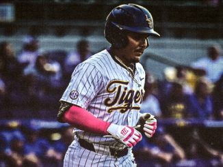Baseball player in a white pinstripe Tigers uniform with pink sleeves, wearing a helmet and running on the field with a crowd in the stands behind.