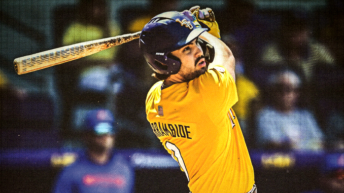 Cricketer wearing a yellow jersey and helmet mid-swing with a bat during a match, looking focused in action.