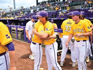 LSU Tigers baseball players in yellow jerseys hug near the dugout, purple caps visible and numbers 40 and 33 on jerseys.
