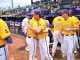 LSU Tigers baseball players in yellow jerseys hug near the dugout, purple caps visible and numbers 40 and 33 on jerseys.