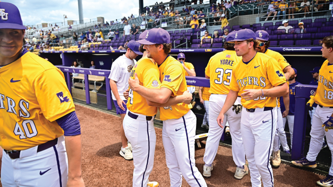 LSU Tigers baseball players in yellow jerseys hug near the dugout, purple caps visible and numbers 40 and 33 on jerseys.