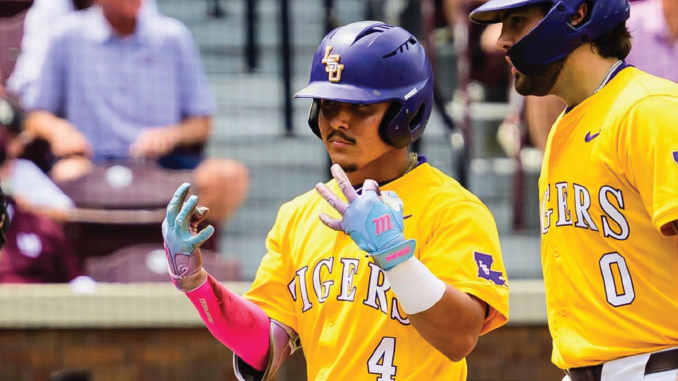 Two LSU Tigers baseball players in yellow jerseys with purple helmets share a high-five on the field; one wears number 4 and pink batting gloves.