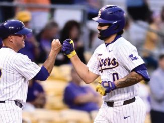 Two baseball players in white pinstriped uniforms high-fiving on the field, both wearing purple helmets.