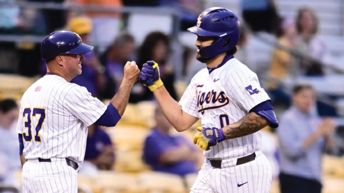 Two baseball players in white pinstriped uniforms high-fiving on the field, both wearing purple helmets.