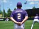Baseball player Johnson, wearing a purple jersey with number 2, stands with hands clasped behind his back on a sunny practice field as teammates train in the background.