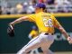 Baseball pitcher in a yellow jersey with 'COWAN' and number 26 throws a pitch on the mound, glove raised left, ball in right hand