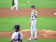 Baseball pitcher on the mound in a white uniform, ball in midair as the catcher crouches in front of home plate.