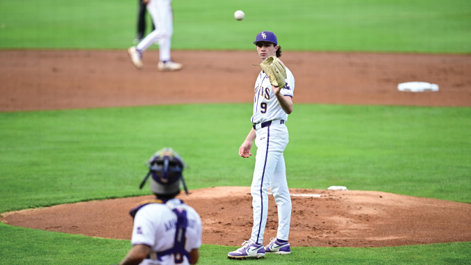 Baseball pitcher on the mound in a white uniform, ball in midair as the catcher crouches in front of home plate.
