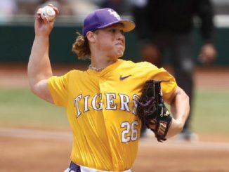 Female baseball pitcher in a yellow Tigers uniform throwing a pitch, glove on her left hand, number 26 visible.