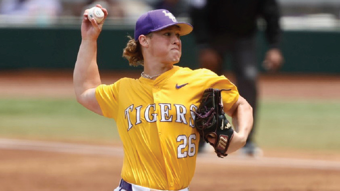 Female baseball pitcher in a yellow Tigers uniform throwing a pitch, glove on her left hand, number 26 visible.