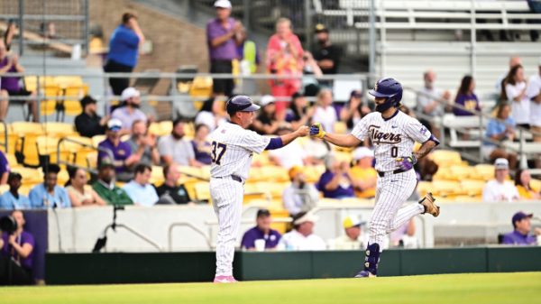 Two baseball players in white pinstriped uniforms high-five on the field as fans sit in yellow seats behind them.