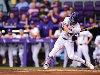 Baseball player in white pinstripe uniform swinging at a pitch at home plate with a purple stadium background