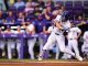 Baseball player in white pinstripe uniform swinging at a pitch at home plate with a purple stadium background