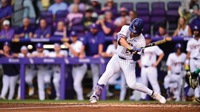 Baseball player in white pinstripe uniform swinging at a pitch at home plate with a purple stadium background