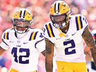 LSU football players wearing white jerseys with purple numbers 42 and 2 walk on the field during a game.