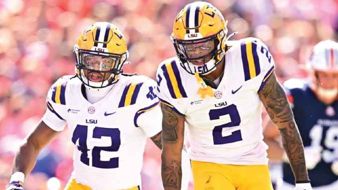 LSU football players wearing white jerseys with purple numbers 42 and 2 walk on the field during a game.